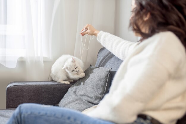 Jugando con un gato. Una mujer con un suéter blanco jugando con su linda mascota.