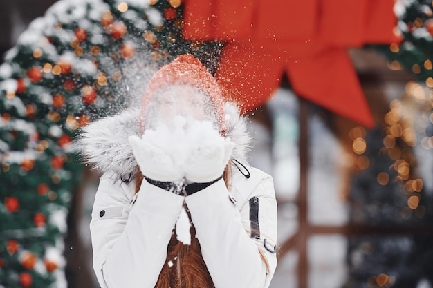 Jugando con nieve Mujer joven feliz de pie al aire libre y celebrando las fiestas navideñas