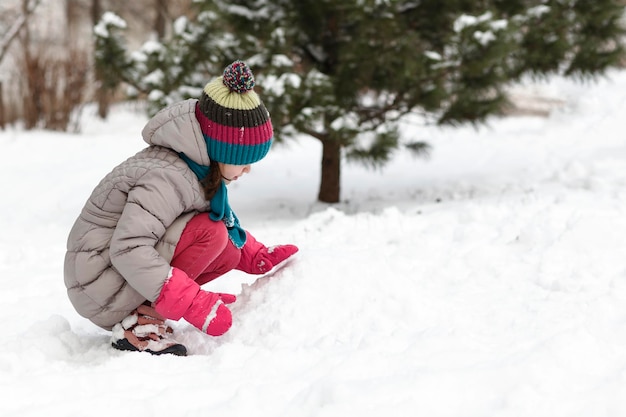 Jugando en la nieve la niña en traje de invierno impermeable con guantes  juega en la nieve