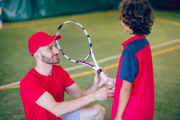 Jugando tenis. Entrenador con gorra roja y niño con raqueta de tenis.