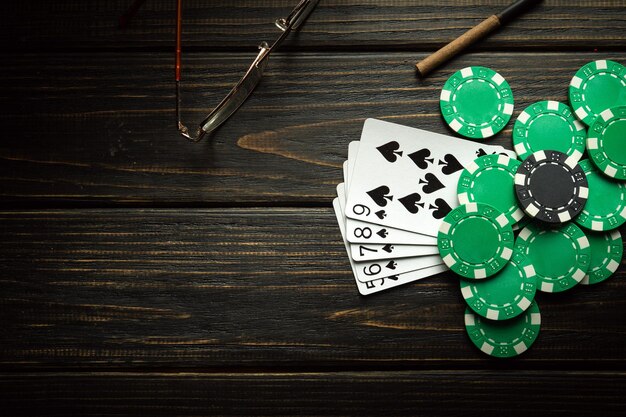 Jugar a las cartas con una combinación ganadora de straight flush y fichas en una mesa vintage negra en un club de póquer Copiar espacio para publicidad