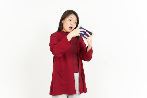 Jugar juego móvil en el teléfono inteligente de la hermosa mujer asiática con camisa roja aislado en blanco