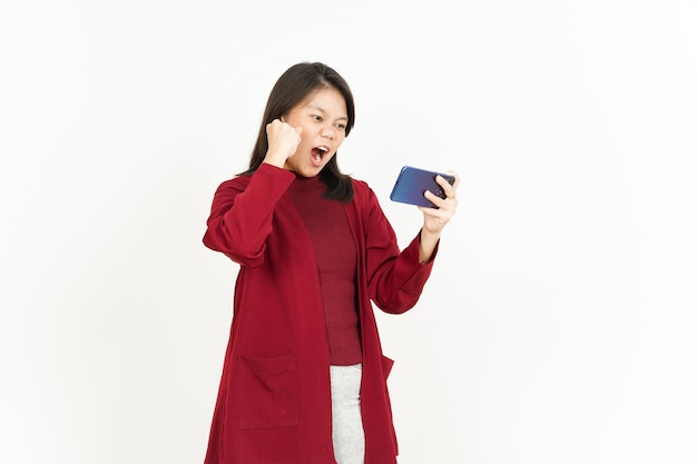 Jugar juego móvil en el teléfono inteligente de la hermosa mujer asiática con camisa roja aislado en blanco