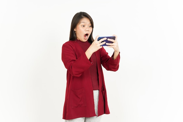 Jugar juegos móviles en el teléfono inteligente de una hermosa mujer asiática con camisa roja aislada en blanco