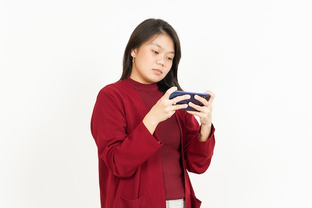 Jugar juegos móviles en el teléfono inteligente de una hermosa mujer asiática con camisa roja aislada en blanco