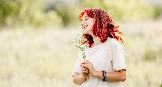 Jugendlich Mädchen mit dem roten Haar an der Natur, die mit Blumenstrauß in den Händen lächelt Hübsche junge Frau im sonnigen Bereich