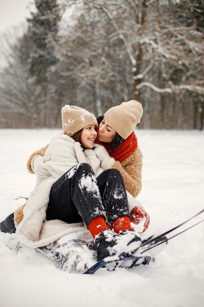 Jugendlich Mädchen und ihre Mutter, die im Winterpark einen Schlitten reiten