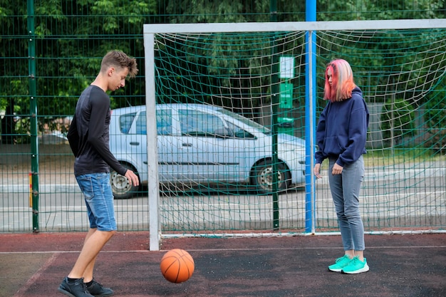 Jugendliche Jungen und Mädchen, die zusammen Straßenbasketball spielen, Jugend mit trendigen Frisuren, die im Freien spielen. Aktiver gesunder Lebensstil, Hobbys und Freizeit, Konzept für Teenager