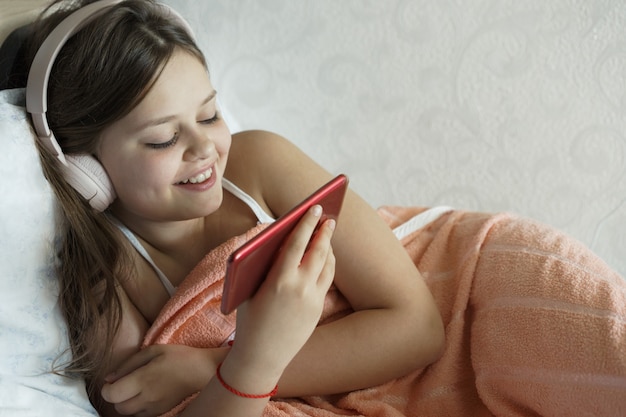 Foto jugendliche liegt im bett mit kopfhörern und einem telefon