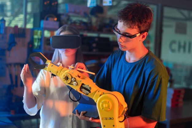 Jugendliche machen Experimente in der Robotik in einem Labor. Junge mit Schutzbrille benutzt Tablet und Mädchen