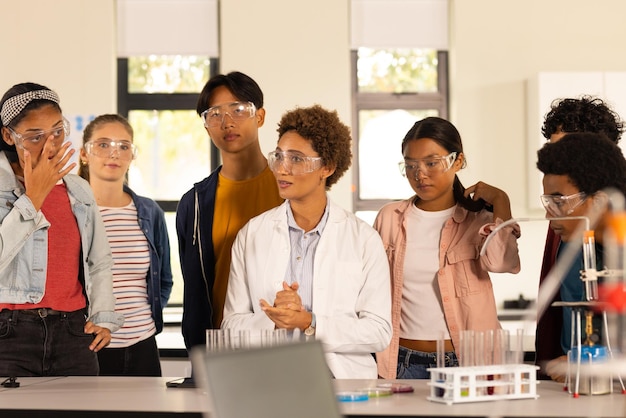 Jugendliche mit Schutzbrille hören dem Lehrer im naturwissenschaftlichen Unterricht an der Highschool zu