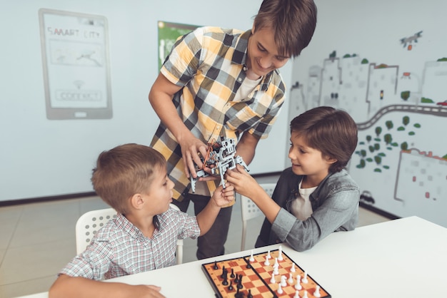 Jugendlicher, der zwei sitzenden Jungen Roboter zeigt.