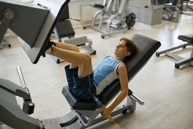 Jugendlicher Junge trainiert Beine an Sportgeräten im Fitnessstudio
