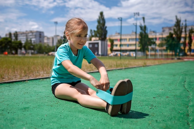 Jugendliches Mädchen, das Übungen mit Fitness-Widerstandsband auf öffentlichem Sportplatz im Stadtsport macht