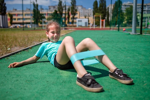 Jugendliches Mädchen, das Übungen mit Fitness-Widerstandsband auf öffentlichem Sportplatz im Stadtsport macht