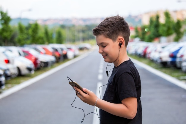 Jugendlichjunge in der zufälligen Kleidung hörend Musik an seinem Handy.