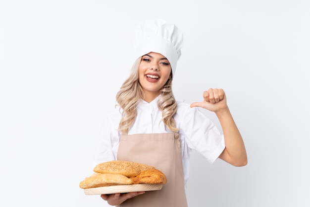 Jugendlichmädchen in der Chefuniform. Weiblicher Bäcker, der eine Tabelle mit einigen Broten über lokalisiertem weißem Hintergrund stolz und selbstzufrieden hält