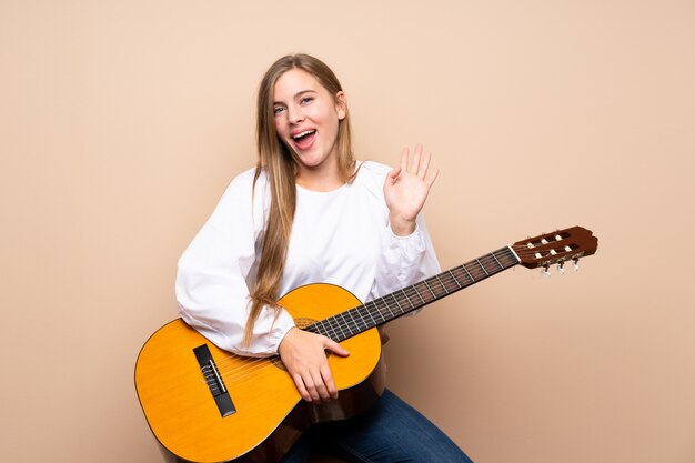 Jugendlichmädchen mit Gitarre begrüßend mit der Hand mit glücklichem Ausdruck