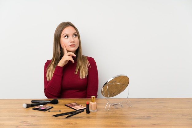 Jugendlichmädchen mit Make-uppalette und Kosmetik in einer Tabelle eine Idee denkend