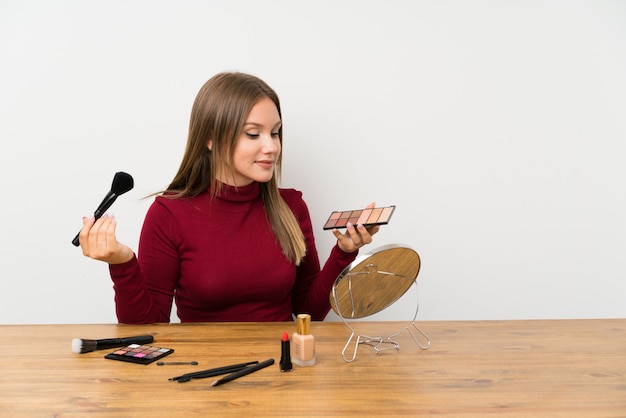 Jugendlichmädchen mit Make-uppalette und Kosmetik in einer Tabelle