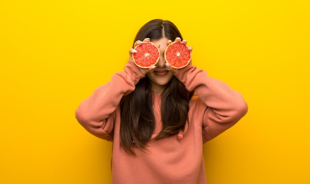 Jugendlichmädchen mit rosa Sweatshirt auf dem gelben Hintergrund, der orange Scheiben als Gläser trägt
