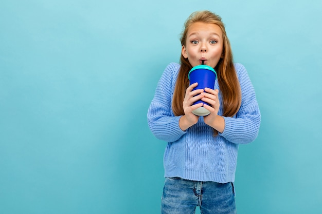 Jugendlichmädchen trinkt glücklich durch einen Strohhalm von einem Glas auf einem blauen Hintergrund