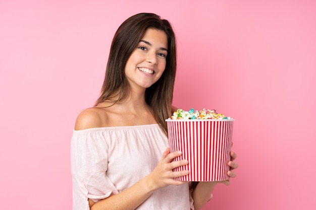Jugendlichmädchen über der lokalisierten rosa Wand, die einen großen Eimer Popcorn hält