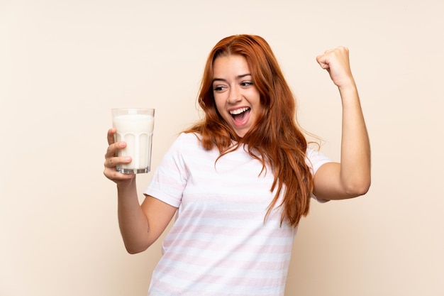 Jugendlichrothaarigemädchen, das ein Glas Milch feiert einen Sieg hält