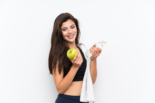 Jugendlichsportmädchen über lokalisierter weißer Wand mit einem Apfel und einer Flasche Wasser