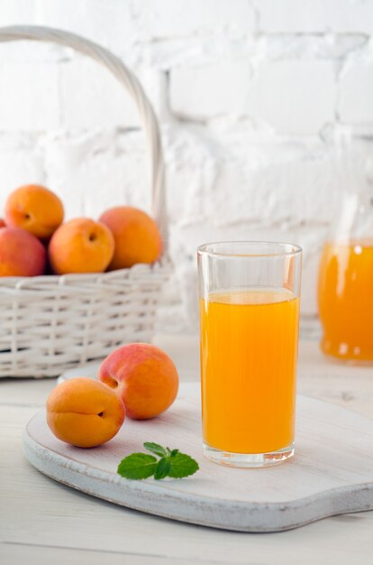 Jugo de albaricoque en vidrio y albaricoques maduros en canasta blanca sobre fondo de pared de ladrillo blanco con espacio para copiar el texto. Enfoque selectivo. De cerca.