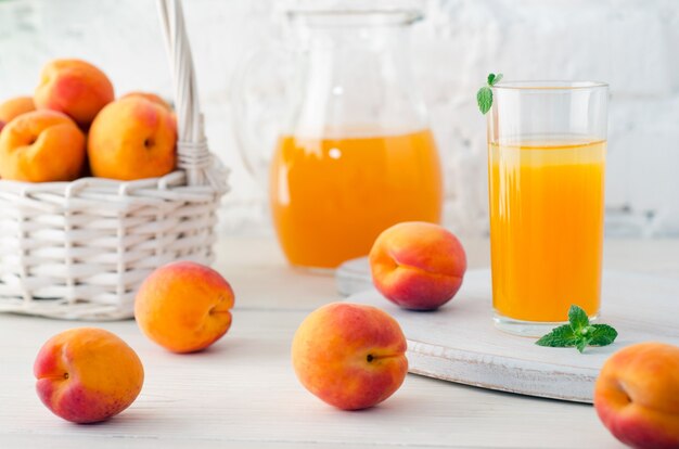 Jugo de albaricoque en vidrio y decantador con albaricoques maduros en mesa de madera sobre fondo de pared de ladrillo blanco. De cerca.