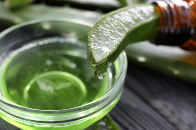 Jugo de aloe vera que gotea de la hoja verde en un tazón, primer plano