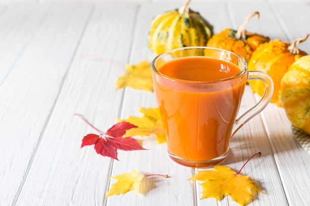 Jugo de calabaza fresca en vaso de vidrio, calabazas y hojas de arce caídas. Concepto de bebida de otoño