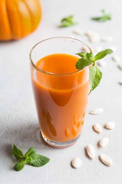 Jugo de calabaza fresco en vaso alto decorado con hojas de menta y semillas de calabaza de cerca sobre fondo gris