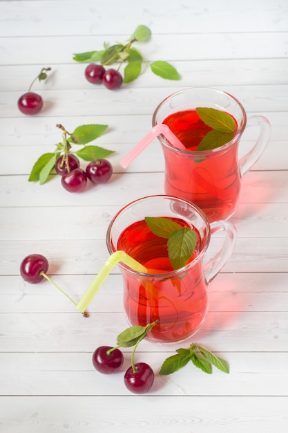 Jugo de cereza con hojas de menta y cerezas frescas en una mesa de madera blanca