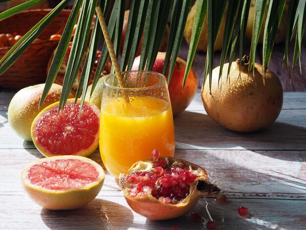 Jugo de cítricos frescos y frutas en una rama de palma de mesa de madera