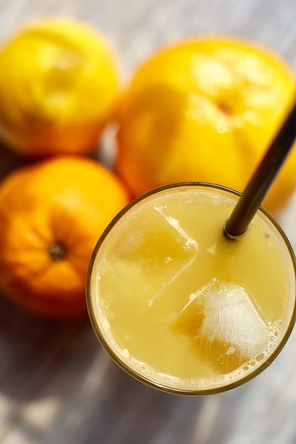 Jugo fresco en un vaso con hielo sobre la mesa y naranjas