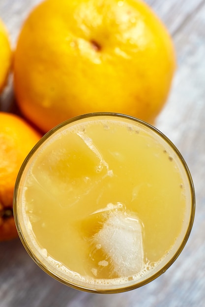 Jugo fresco en un vaso con hielo sobre la mesa y naranjas