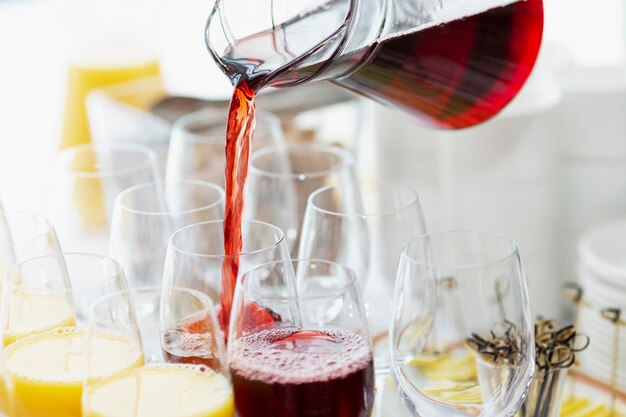 El jugo de frutos rojos se vierte de una jarra en un vaso en un banquete. De cerca. Celebraciones y fiestas.