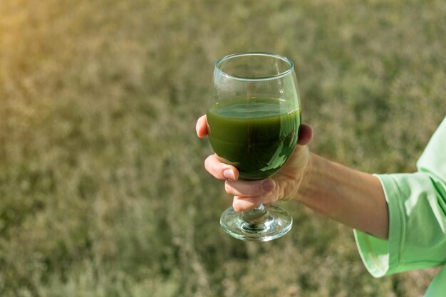 Jugo de germen de trigo, té matcha. Comida sana en la mano. Una mujer bebe al aire libre.