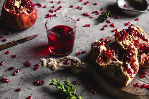 Jugo de granada roja en un vaso, granada madura y cortada y una ramita de menta sobre un fondo de hormigón gris. Concepto de alimentos saludables, antioxidantes y vitaminas. Endecha plana Vista superior.