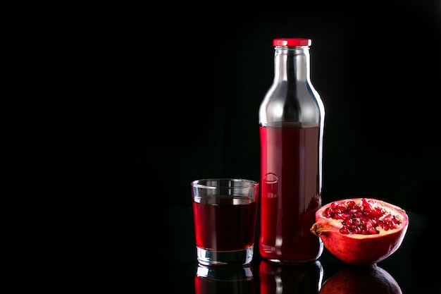 El jugo de granada en un vaso, botella y la mitad de la granada. Vitaminas, alimentos y bebidas saludables.