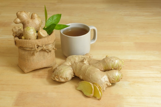 Jugo de jengibre fresco en una taza con hojas de naranja y hojas de pandan sobre fondo blanco.