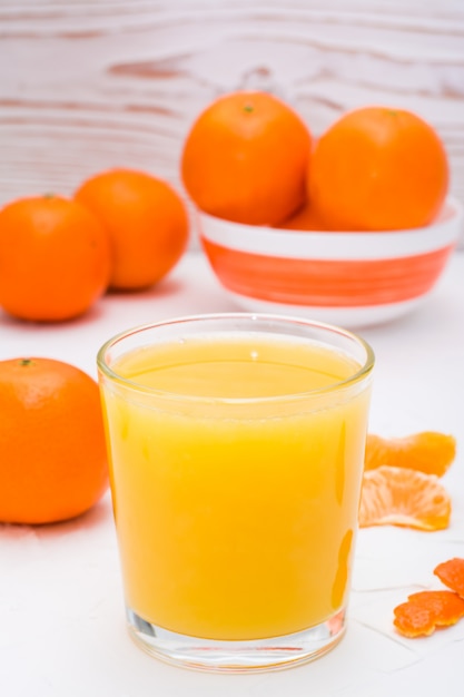 Jugo de mandarina en un vaso y mandarinas maduras sobre una mesa