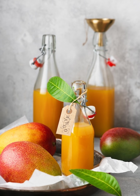 Jugo de mango casero en una botella de vidrio sobre una bandeja de metal con frutas frescas maduras. Bebida saludable de verano