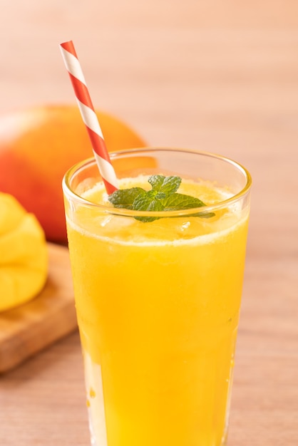 Jugo de mango fresco con pulpa de pulpa picada hermosa y paja sobre fondo de mesa de madera brillante