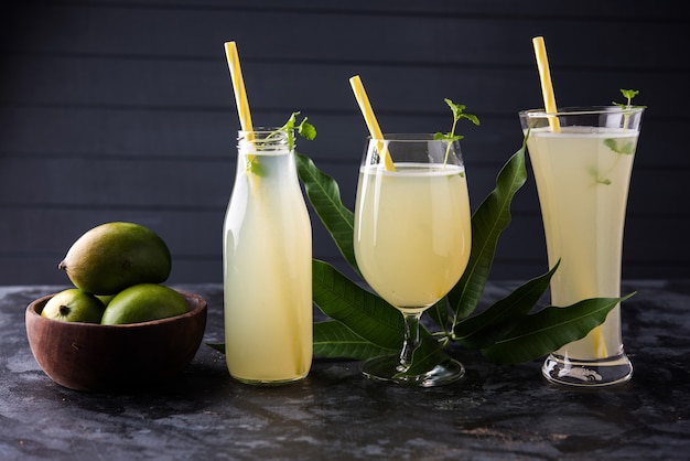 Jugo de mango o Aam Panna o Panha en un vaso transparente con fruta verde entera, enfoque selectivo