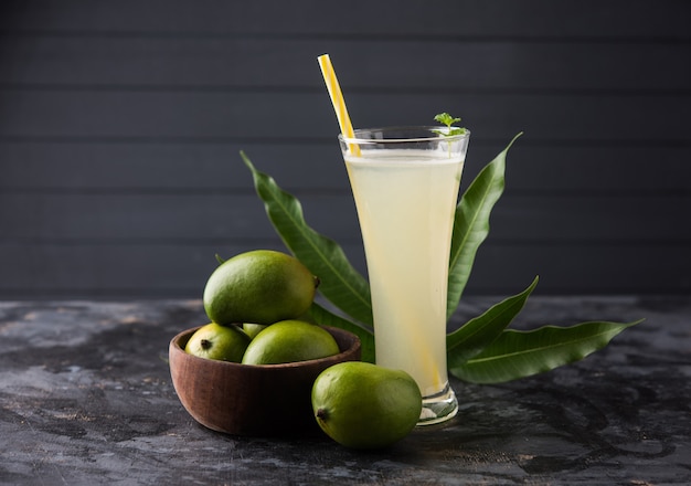 Jugo de mango o Aam Panna o Panha en un vaso transparente con fruta verde entera, enfoque selectivo