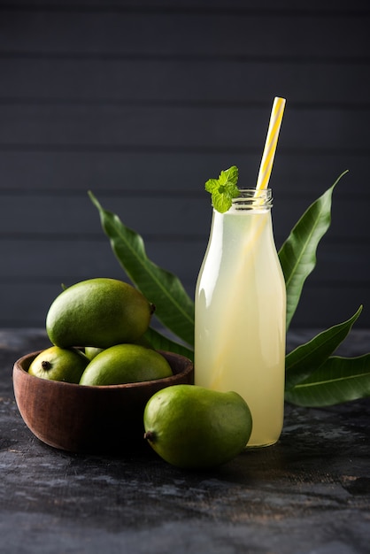 Jugo de mango o Aam Panna o Panha en un vaso transparente con fruta verde entera, enfoque selectivo