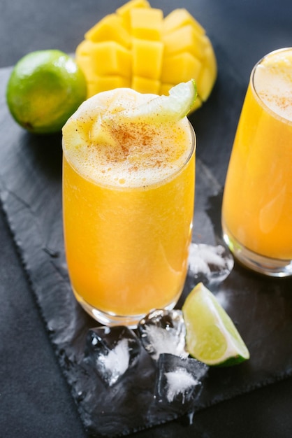 Jugo de mango sobre un fondo oscuro Bebida de verano con hielo y rodajas de mango y lima